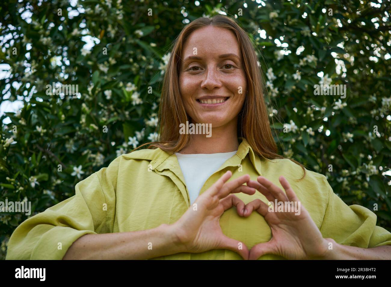 Femme souriante faisant un geste de coeur dans le jardin Banque D'Images