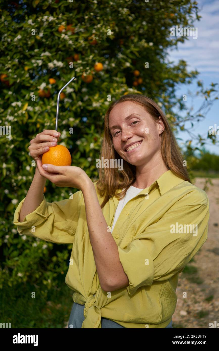 Bonne femme montrant de l'orange avec de la paille en métal réutilisable dans le verger Banque D'Images