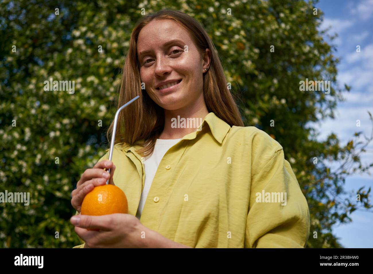 Femme souriante avec de la paille métallique orange et réutilisable dans un verger Banque D'Images