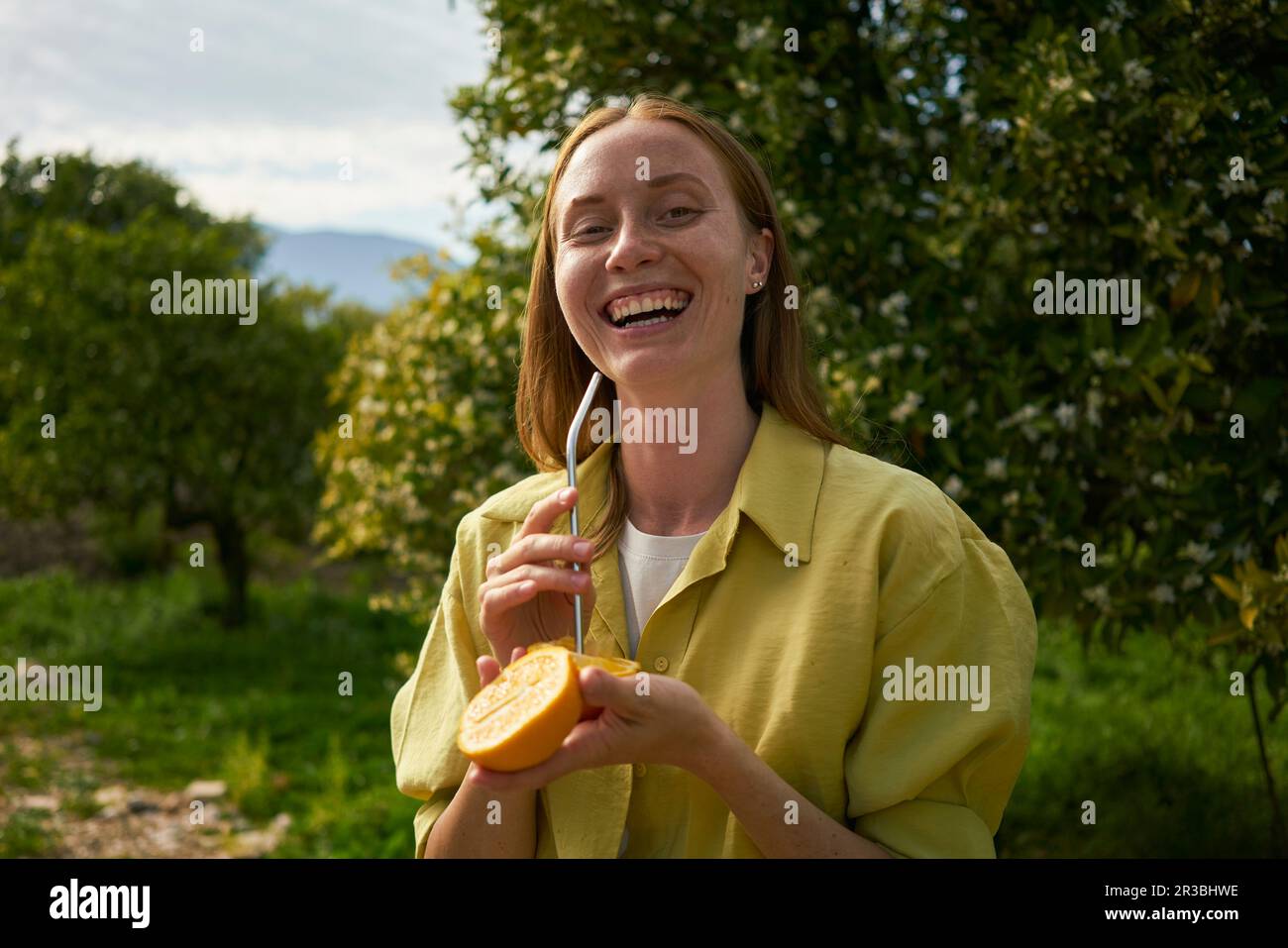 Bonne femme avec de la paille métallique réutilisable et des tranches d'orange au verger Banque D'Images