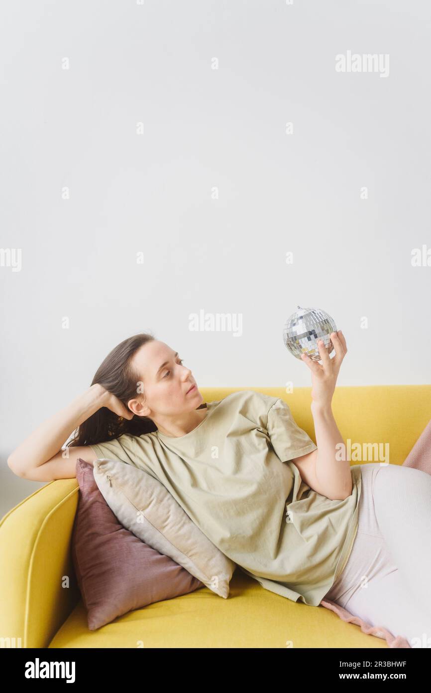 Femme tenant une boule de verre couché sur un canapé jaune Banque D'Images