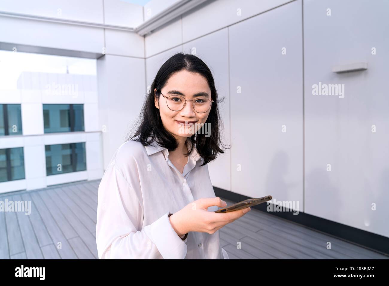 Portrait d'une jeune femme d'affaires avec téléphone mobile sur la terrasse du bâtiment de bureau Banque D'Images