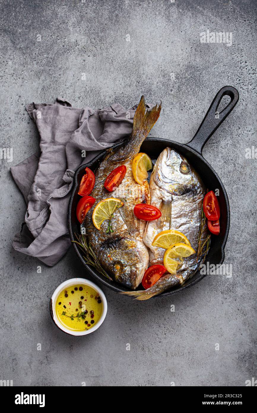 Dorade rôtie au citron, aux herbes et aux tomates dans une poêle en fonte Banque D'Images