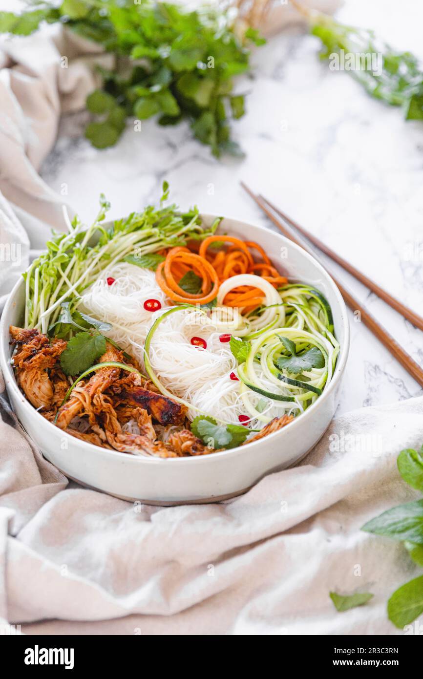 Bol à nouilles de poulet avec courgettes, carottes râpées et herbes fraîches Banque D'Images