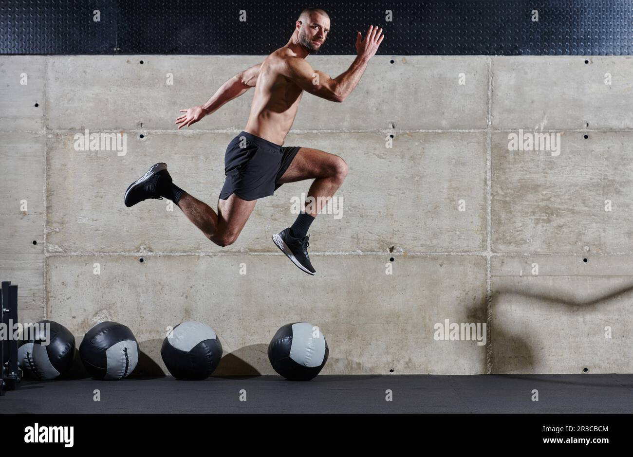 Un homme musclé capturé dans l'air alors qu'il saute dans une salle de sport moderne, mettant en valeur son athlétisme, sa puissance et sa détermination grâce à une forme physique de haute intensité Banque D'Images