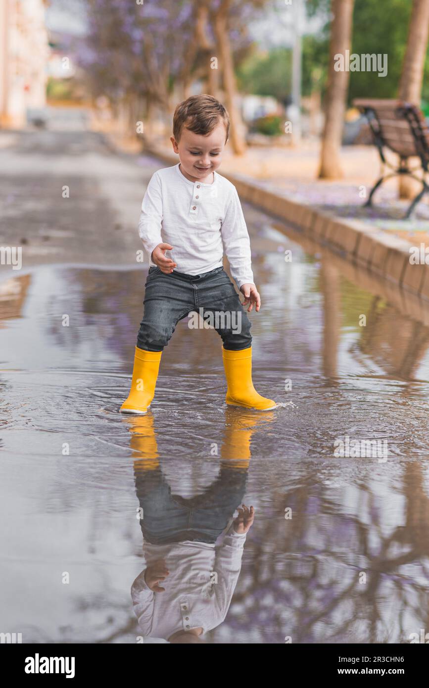 garçon dans des bottes en caoutchouc jaune sautant par-dessus une flaque sous la pluie. Banque D'Images