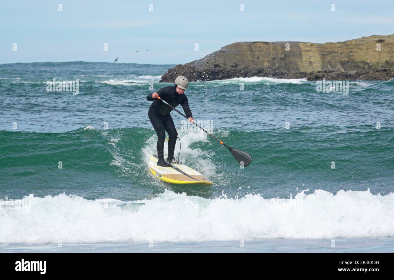 Un paddleboarder de stand-up fait le surf près de Haystack Rock dans Pacific City, Oregon, sur la côte Pacifique de l'Oregon. Banque D'Images