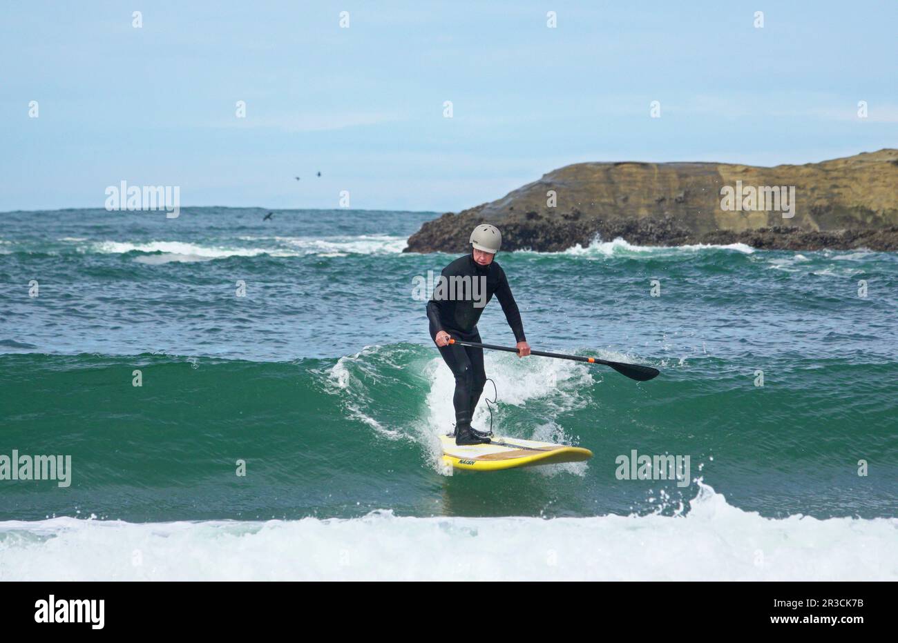Un paddleboarder de stand-up fait le surf près de Haystack Rock dans Pacific City, Oregon, sur la côte Pacifique de l'Oregon. Banque D'Images