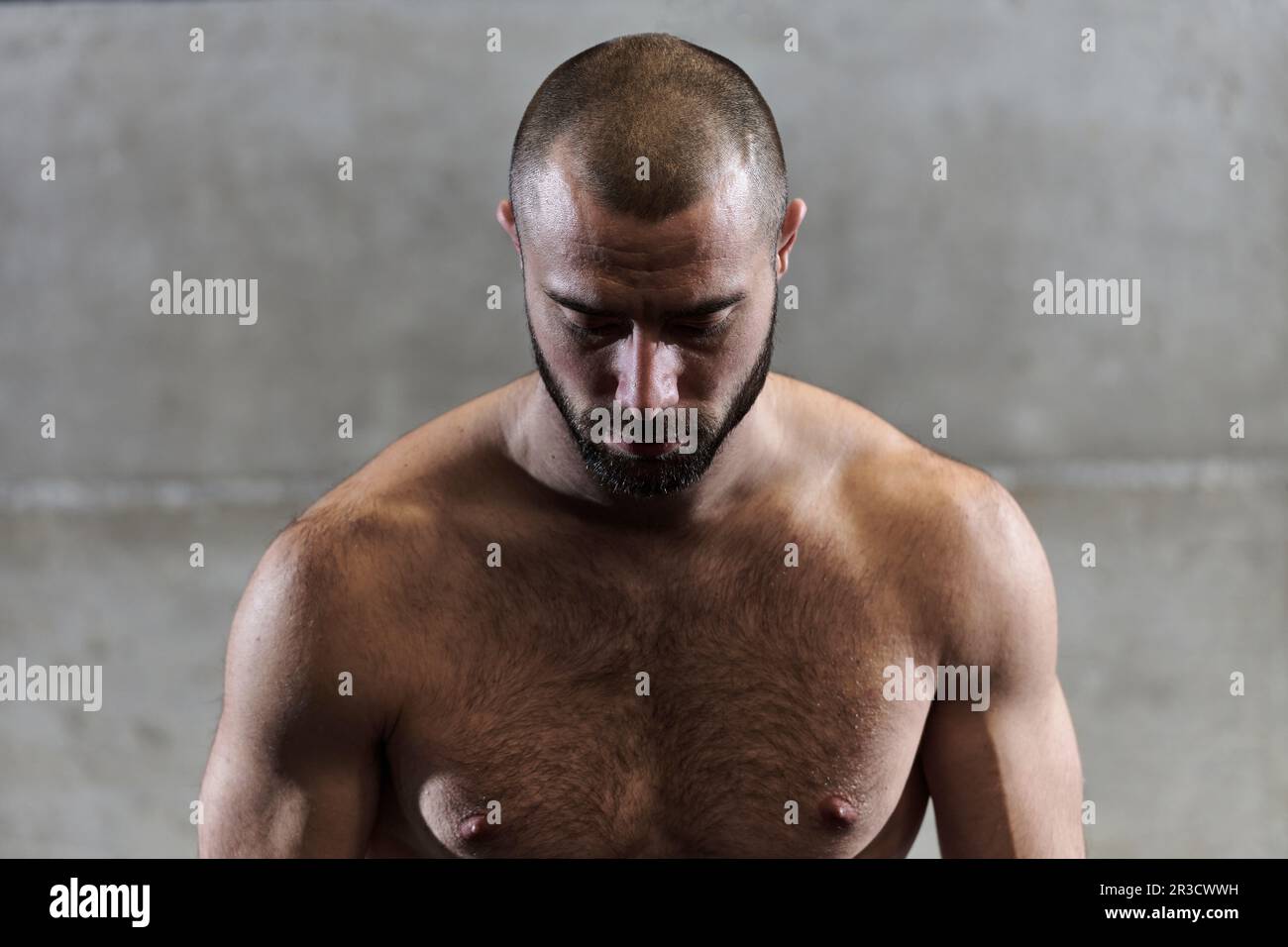 Un homme musclé pose dans la salle de gym, mettant en évidence sa force et son dévouement à la forme physique grâce à un physique impressionnant et à la sueur d'écoute sur son visage. Banque D'Images