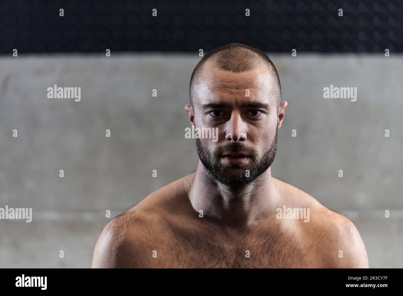 Un homme musclé pose dans la salle de gym, mettant en évidence sa force et son dévouement à la forme physique grâce à un physique impressionnant et à la sueur d'écoute sur son visage. Banque D'Images