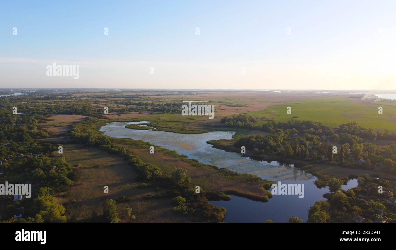 Un drone survole une rivière en agitant entourée d'un village local avec divers bâtiments et marais et marais Banque D'Images