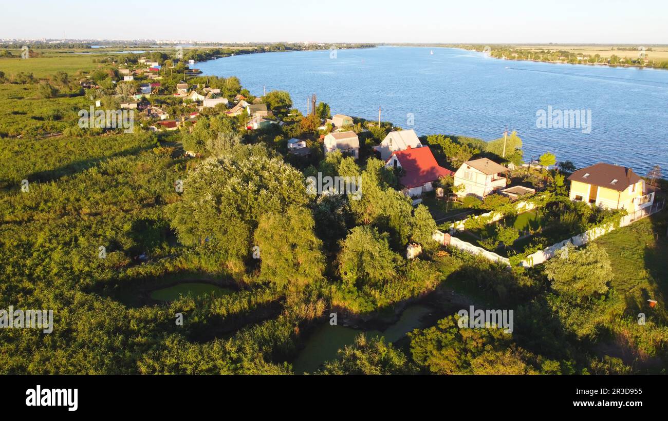 Un drone survole une rivière de couleur bleue entourée d'un village local avec divers bâtiments et un habitat dans les marais et les zones humides Banque D'Images