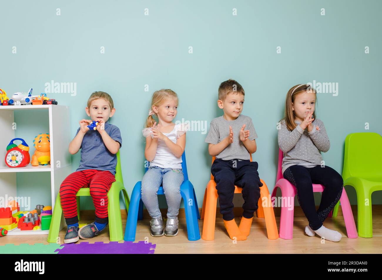 Les enfants sont assis sur les chaises colorées de la maternelle Banque D'Images