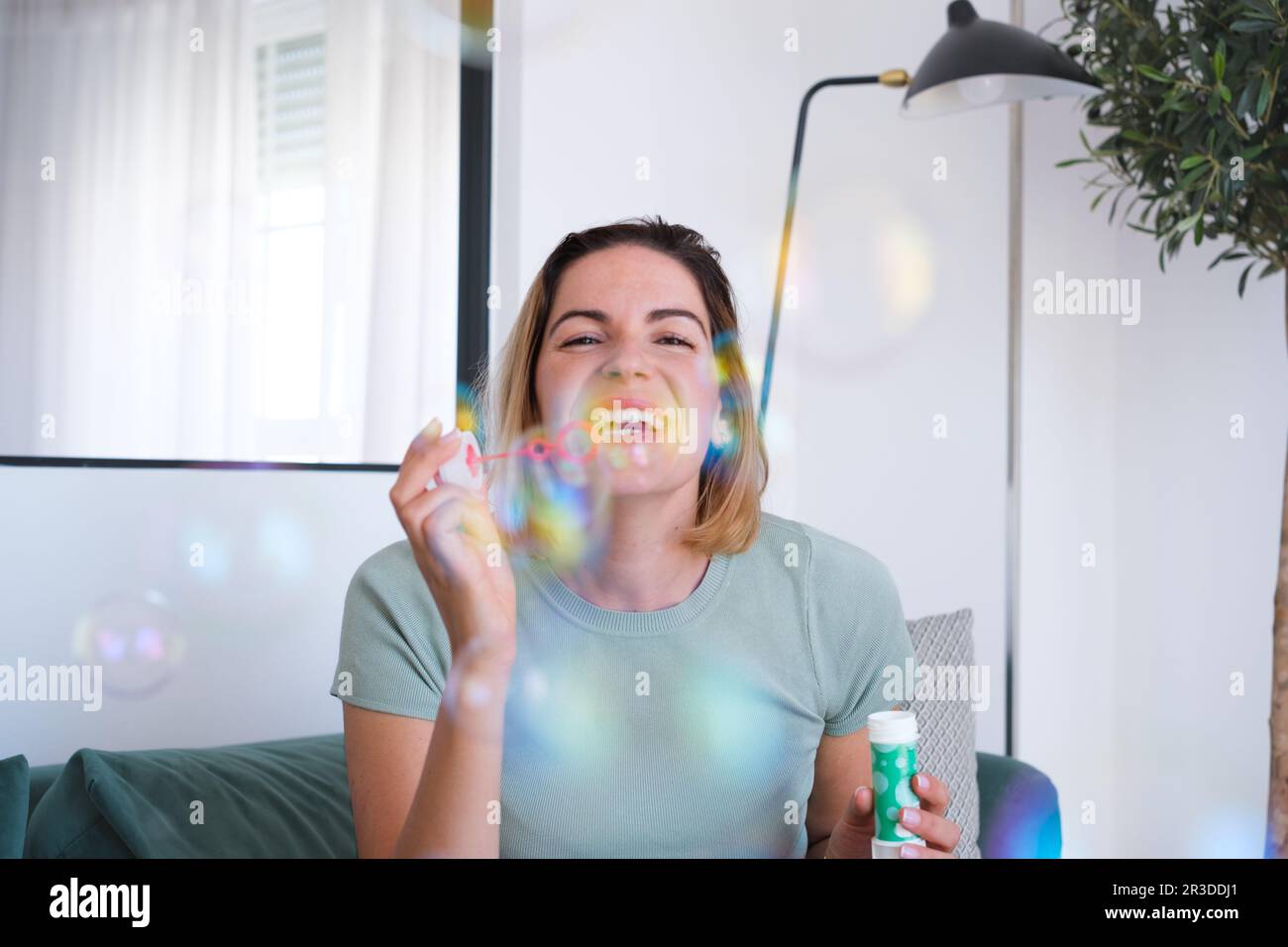 Une jeune femme soufflait de bulles de savon dans son salon. Concept: Amusement, intérieur, divertissement Banque D'Images