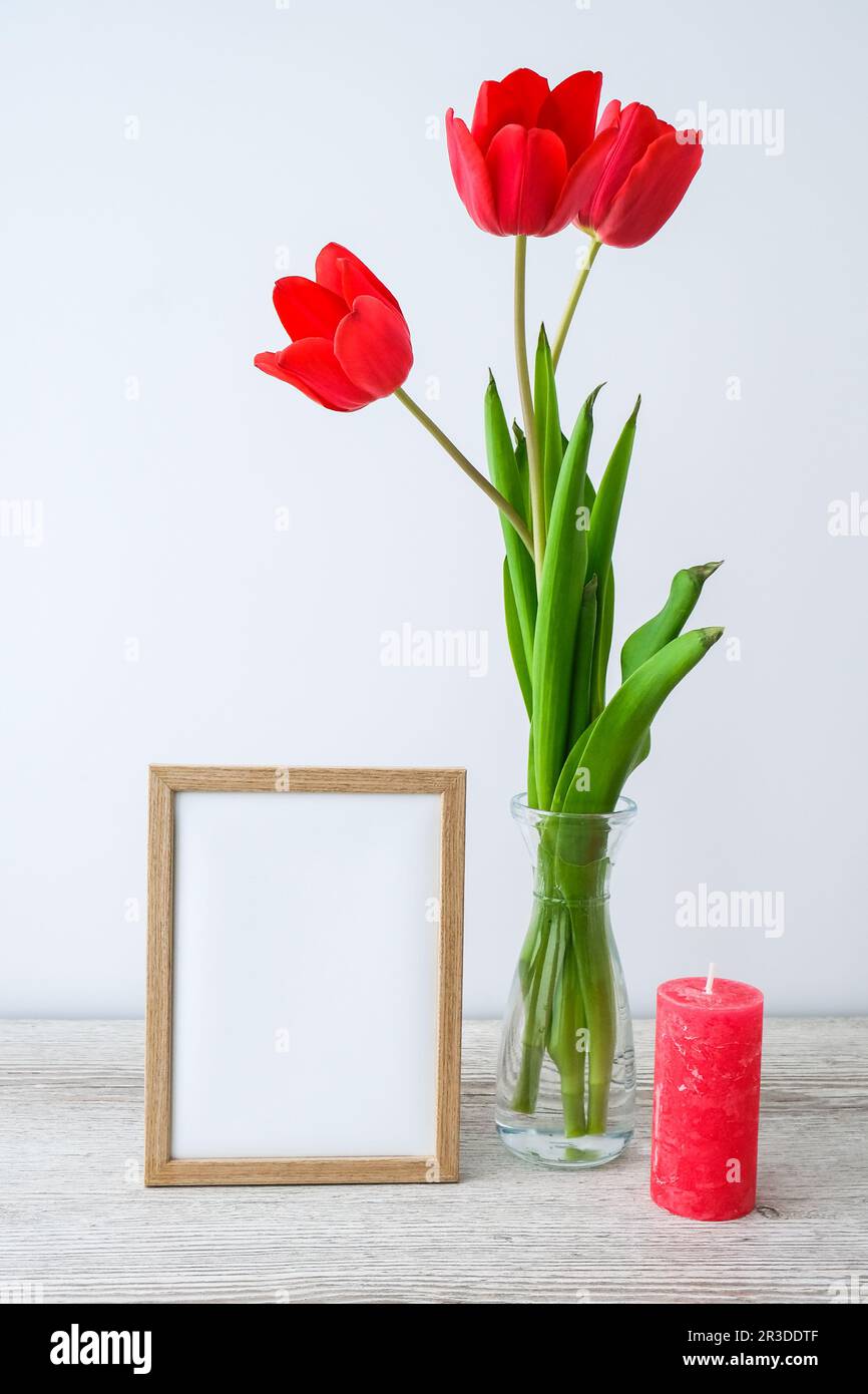 Maquette des fêtes. Fleurs tulipes dans vase en verre avec cadre photo décor sur table en bois arrière-plan mur à la maison, gros plan, Fête des mères Womans Valentines Banque D'Images