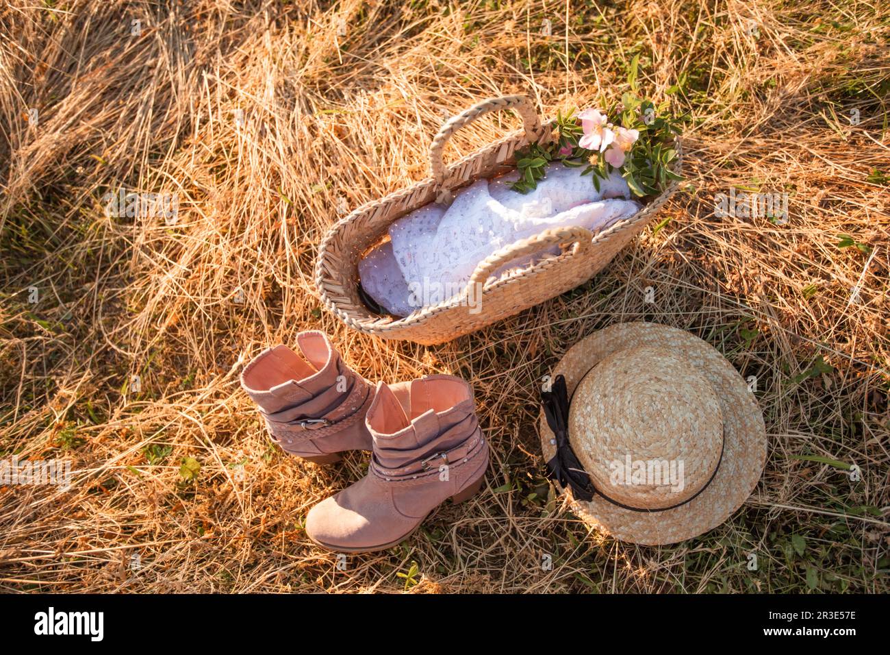 Vue de dessus sac en osier avec tissu blanc à l'intérieur, paire de bottes  roses et chapeau de paille placé près de la pile de foin sec. Photo  extérieure d'été de style