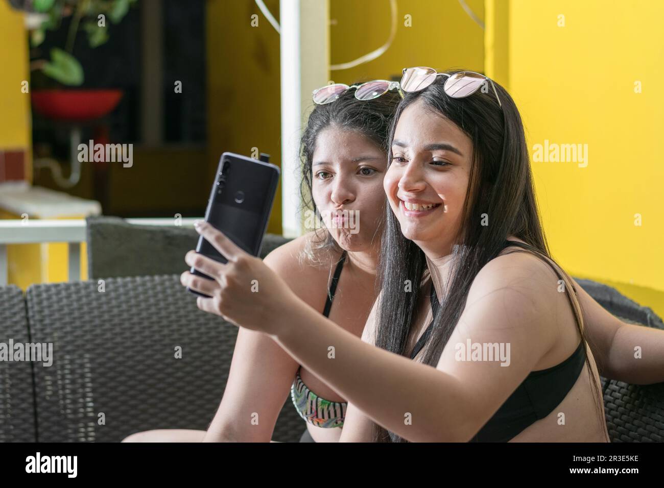 deux belles femmes latines prennent une photo avec leur téléphone cellulaire, rient et font des gestes avec leur bouche Banque D'Images