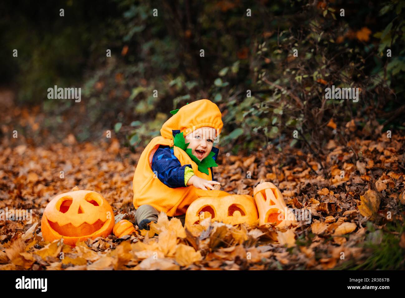 Mignon garçon en costume de citrouille parmi les citrouilles sculptées Banque D'Images