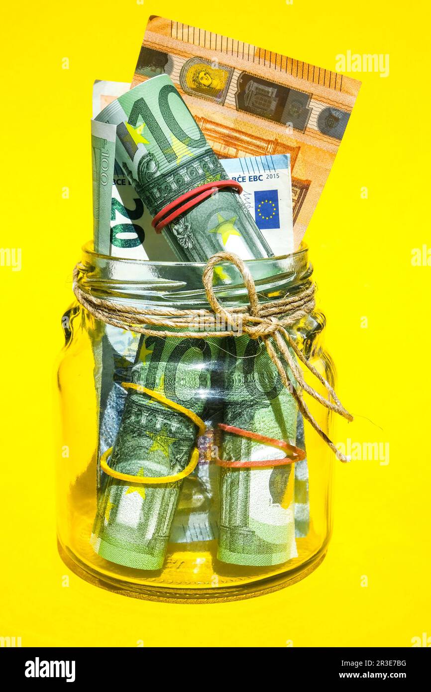 Pots en verre remplis de billets d'euros, économies à l'intérieur de pot en verre, argent isolé sur fond jaune, espace de copie pour le texte. Papier non Banque D'Images