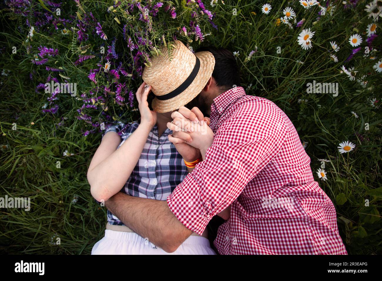Couple romantique embrassant dans le champ d'été avec fleurs sauvages Banque D'Images