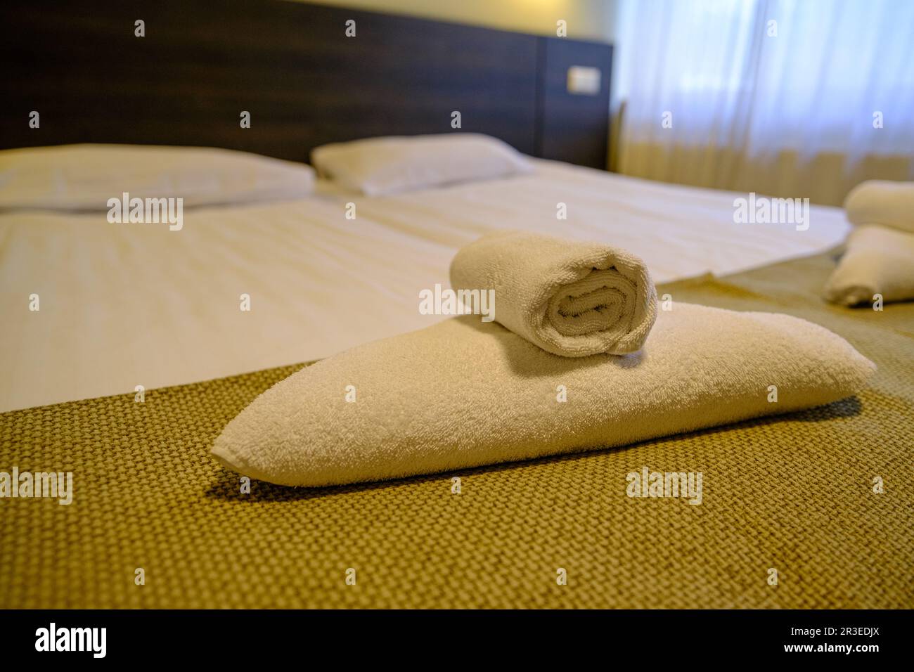 Chambre d'hôtel avec lit fraîchement préparé, draps parfaitement propres et repassés, pile de nouvelles serviettes pliées à la lumière naturelle du soleil. Banque D'Images
