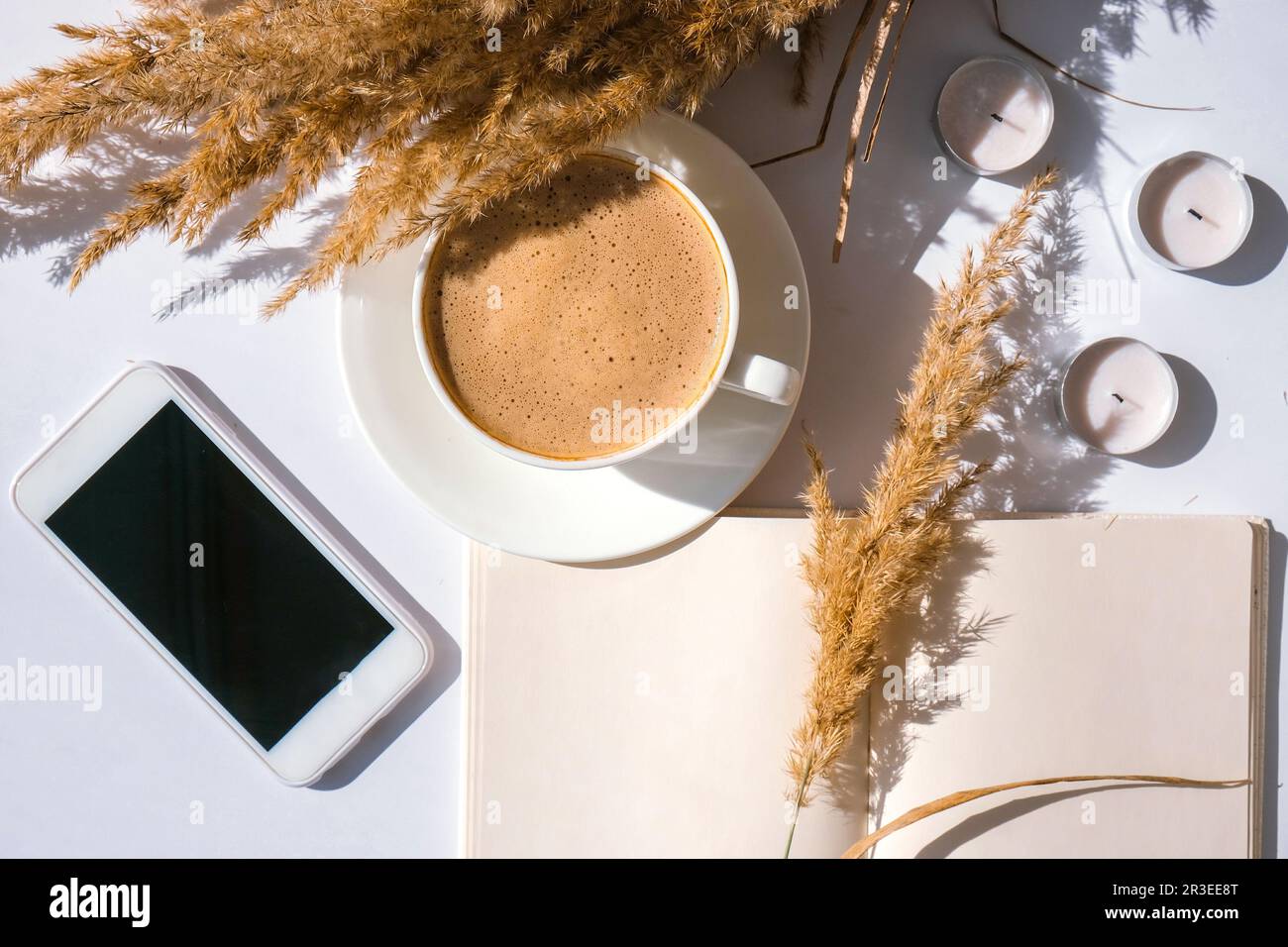 Pampas herbe et tasse blanche avec café. Téléphone portable avec écran noir. Vérifier les médias sociaux boire un cappuccino le matin du petit déjeuner à la maison. FL Banque D'Images