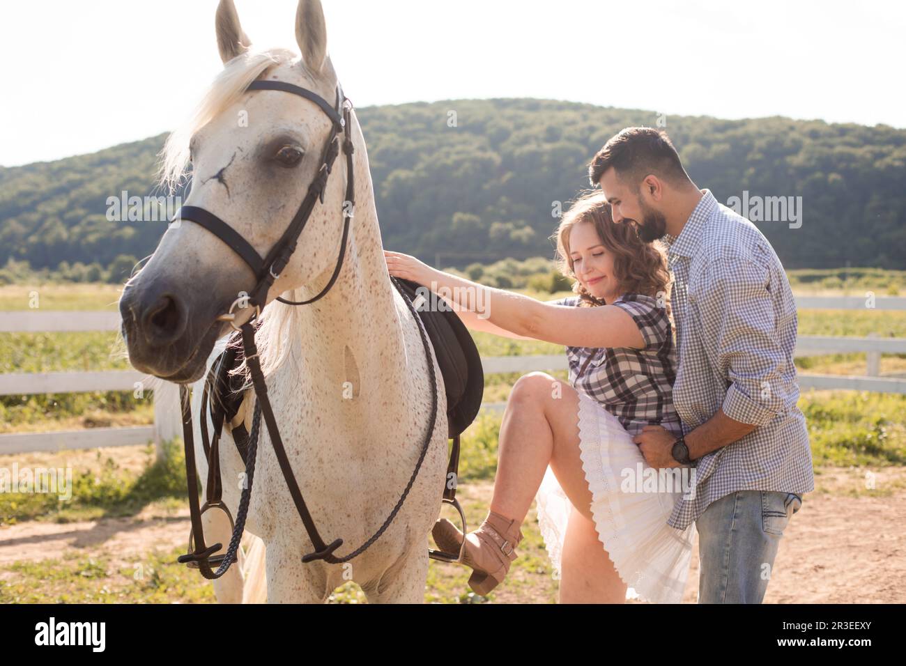 Le jeune homme aide sa femme à monter sur un cheval Banque D'Images