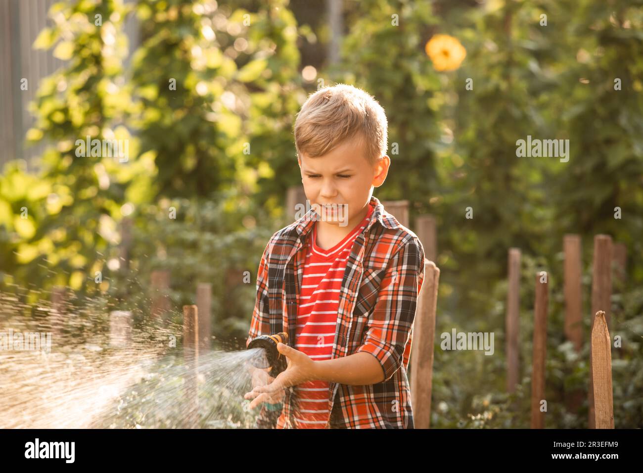 Le garçon arrose le lit de jardin à l'aide d'un tuyau Banque D'Images