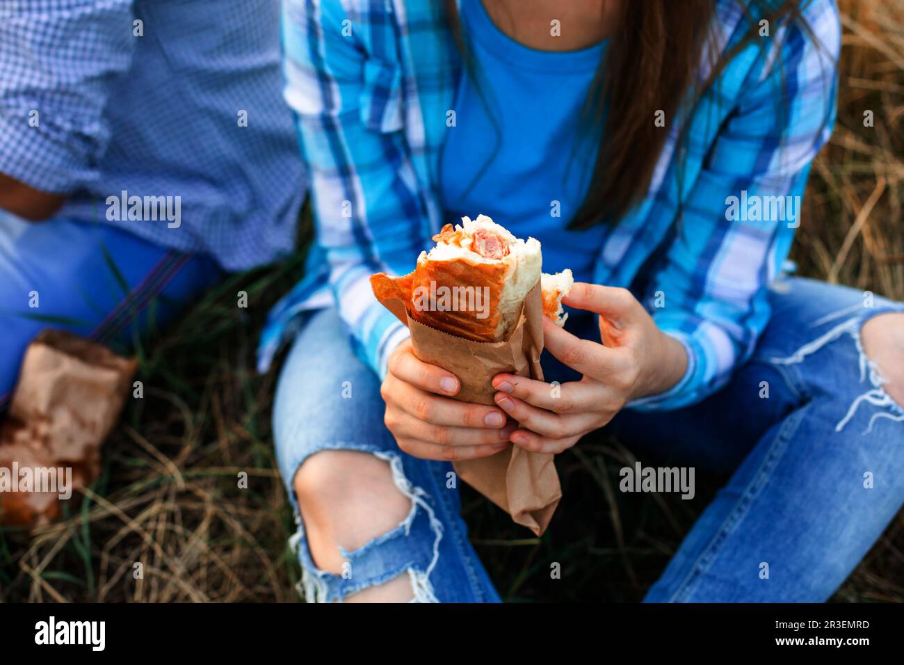 Une femme mange un hamburger à l'extérieur, assis à l'herbe Banque D'Images