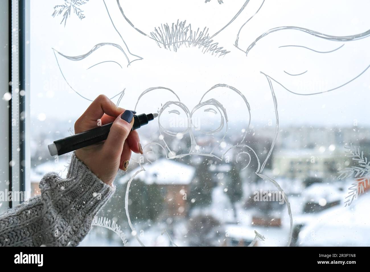 Femme peinture à la main cerf de Noël peint sur verre de fenêtre. Décoration d'hiver de Noël sur la vitre. Motif de cerf blanc. Banque D'Images