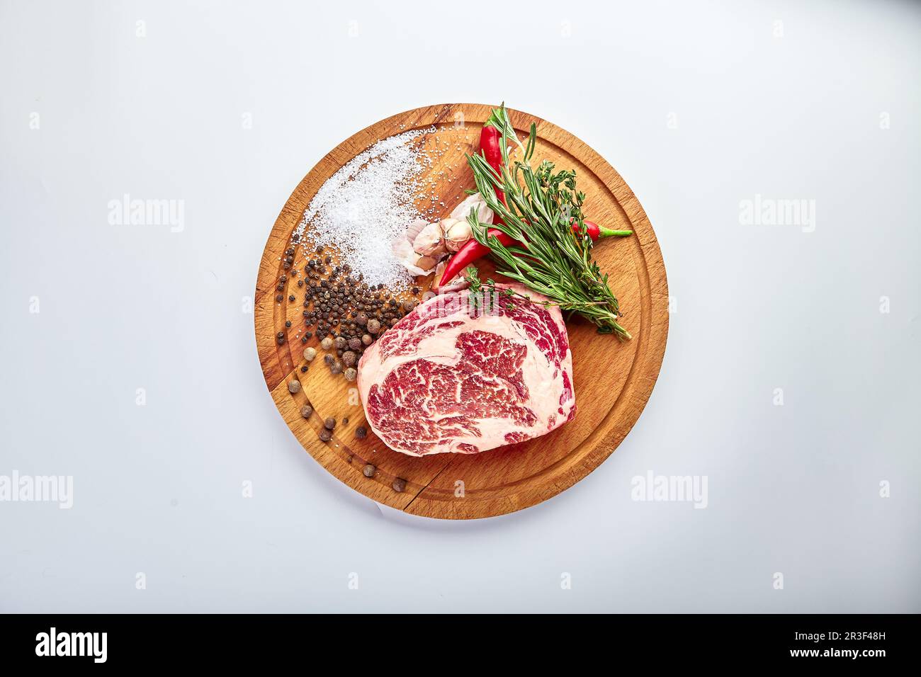 Bifteck de ribeye sur le beurrier avec romarin, poivre et sel sur une table en bois, préparé pour la cuisson. Banque D'Images