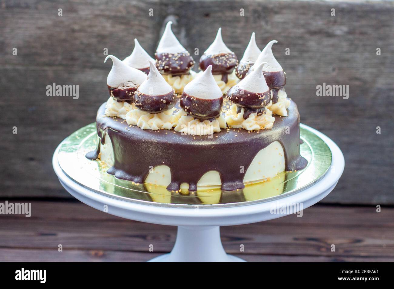 Cheesecake d'anniversaire décoré avec une sauce au chocolat noir fondu, des meringues et des tourbillons de crème au beurre sur le cakestan blanc. Arrière-plan rustique Banque D'Images