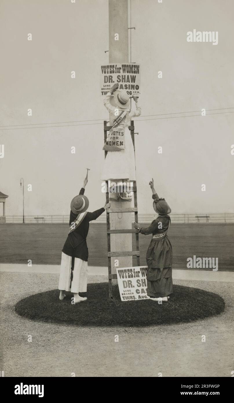 Trois femmes installant un panneau publicitaire d'un événement de suffrage. Banque D'Images