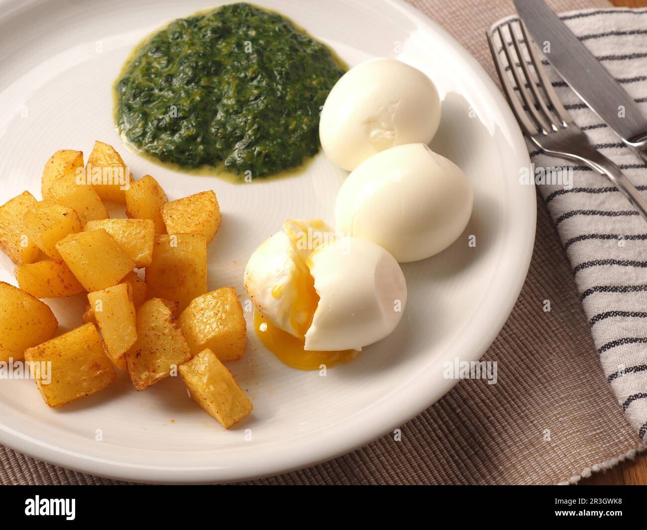 Épinards biologiques servis avec des cubes de pommes de terre épicés et un œuf biologique bouilli sur une assiette blanche. Une alimentation saine Banque D'Images