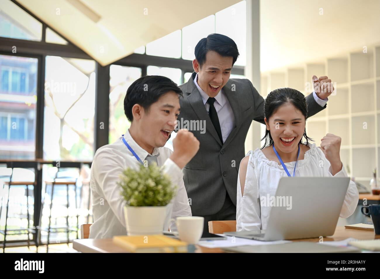 Un groupe d'hommes d'affaires asiatiques surjoyeux regarde un écran d'ordinateur portable, criant avec joie, montrant leurs poings, se réjouissant et célébrant leur rp Banque D'Images