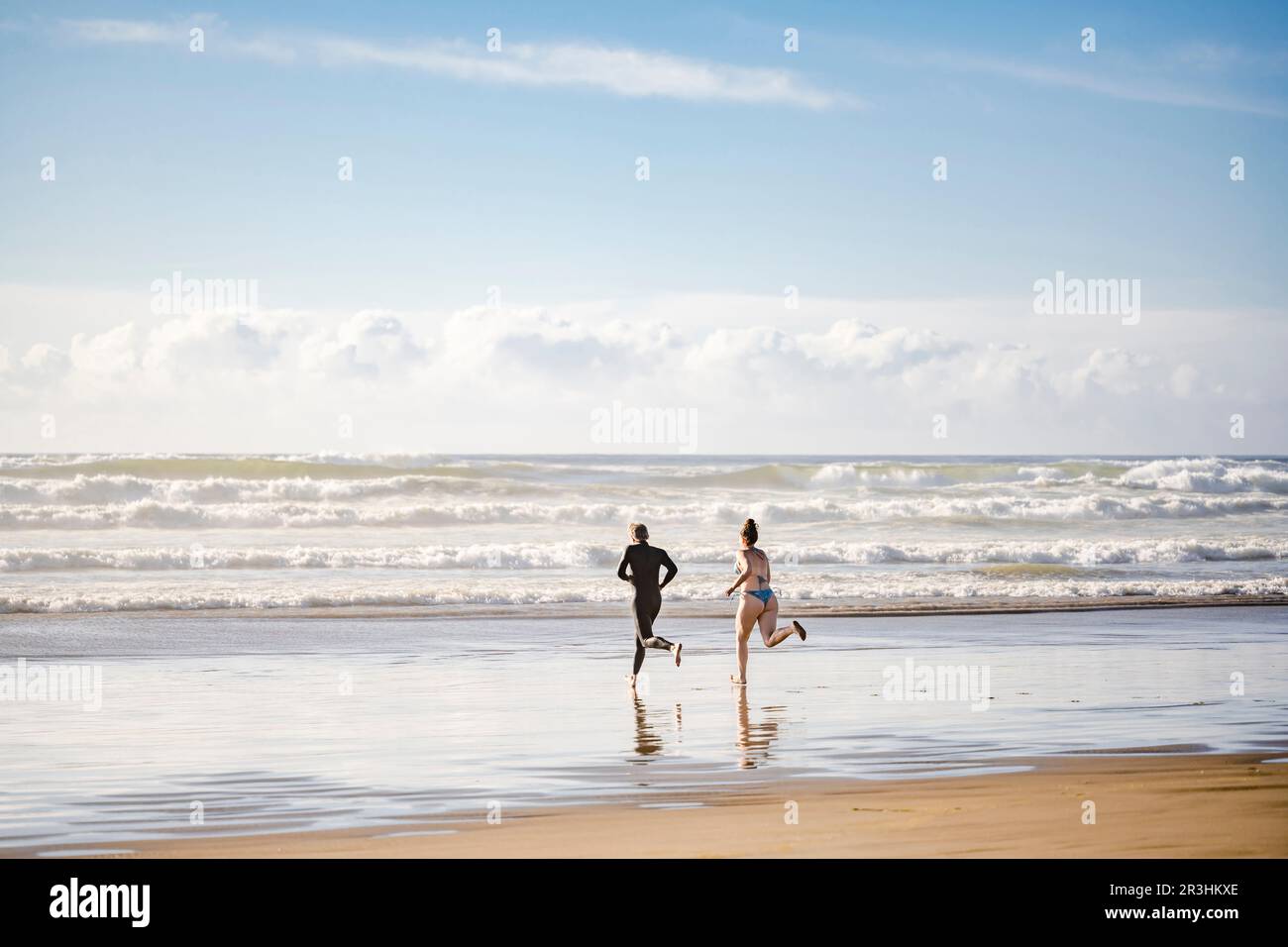 Un couple heureux s'est conduit pour nager dans les vagues du nord-ouest de l'océan Pacifique froid dans les rayons du soleil soluble dans la brume spray respirante sain air frais Banque D'Images
