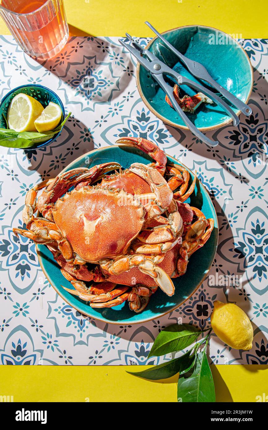 Crabe cuit sur une assiette bleue, citrons, vin de rose sur une table, intensité de lumière du soleil Banque D'Images