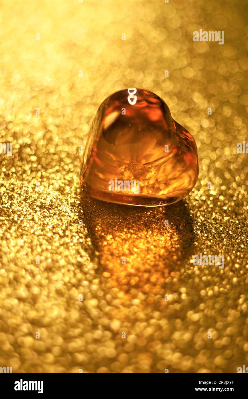 Coeur en verre ambré sur table dorée brillante. Banque D'Images