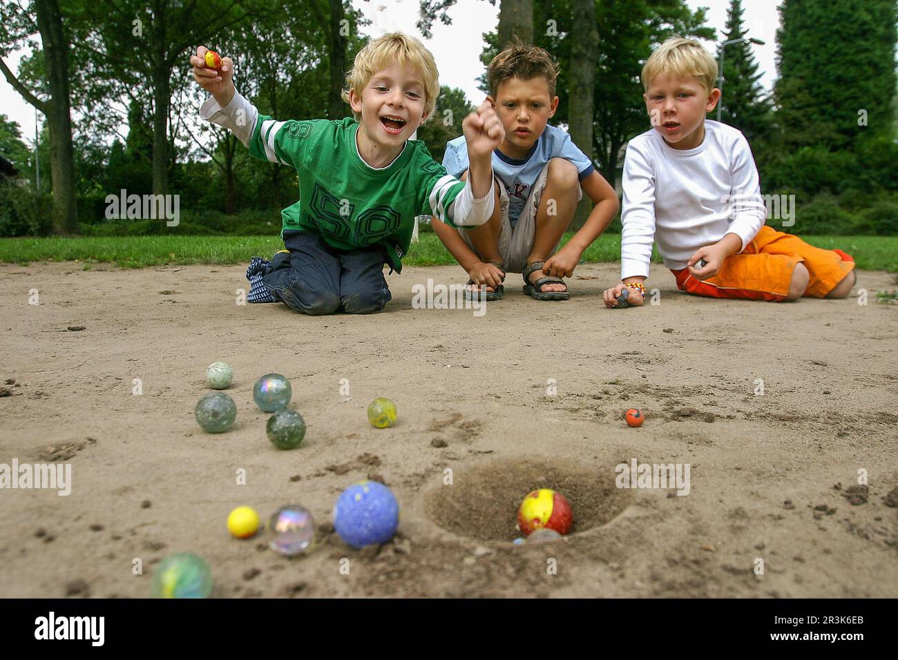 Pays-Bas, dans le village de Huissen, trois garçons jouent à un jeu de billes. Banque D'Images