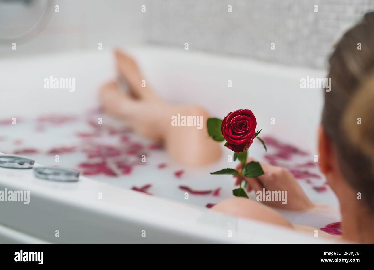 Une femme se détend dans un bain avec du lait et des pétales de rose. Banque D'Images