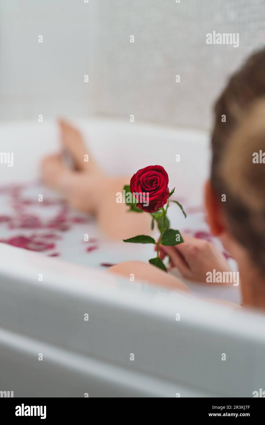 Une femme se détend dans un bain avec du lait et des pétales de rose. Banque D'Images