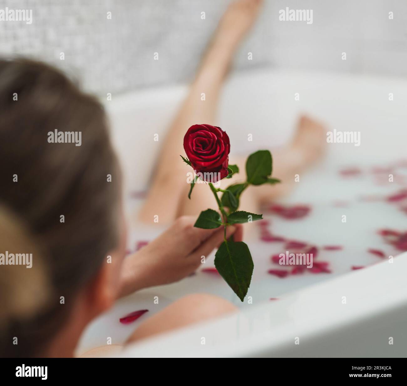 Une femme se détend dans un bain avec du lait et des pétales de rose. Banque D'Images