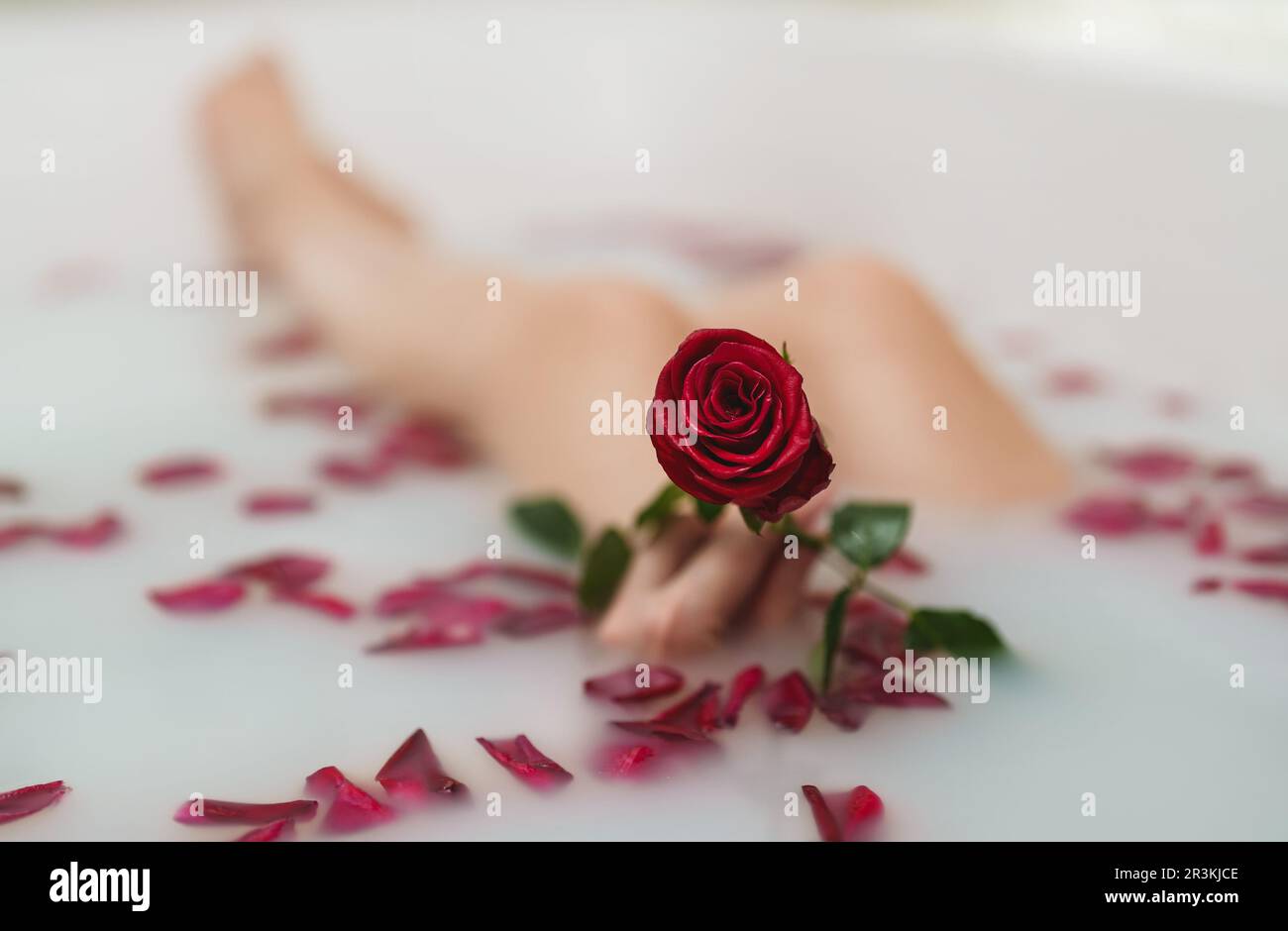 Une femme se détend dans un bain avec du lait et des pétales de rose. Banque D'Images