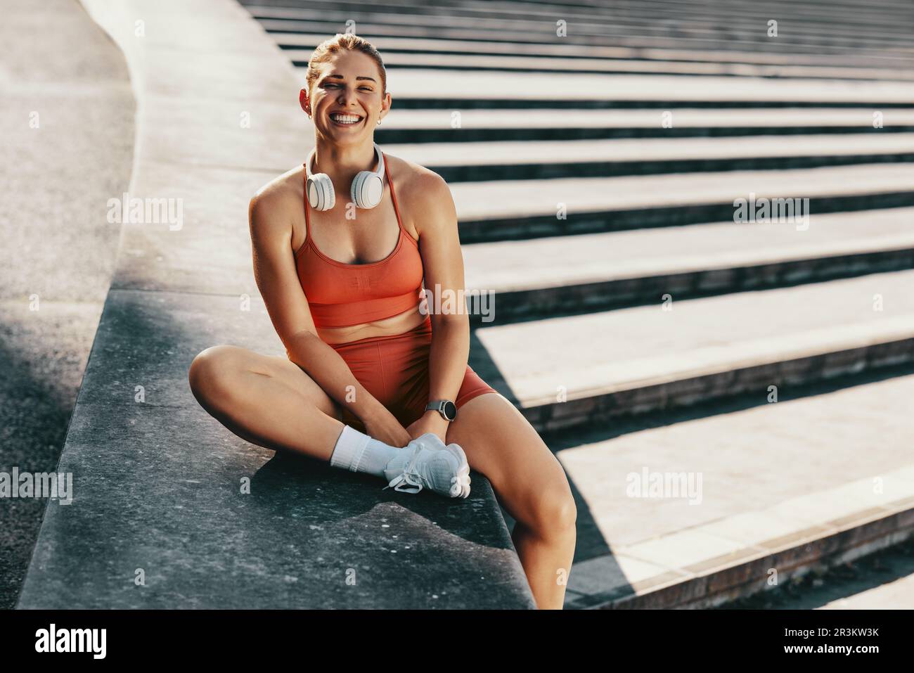 Portrait d'une heureuse femme sportive assise à l'extérieur. Femme sportive prenant une pause de jogging à l'extérieur. Une femme s'entraîner le matin. Banque D'Images