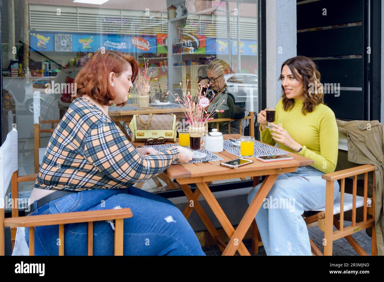 deux jeunes femmes latino-argentines, amis sont assis à l'extérieur de la cafétéria, parlant de boire du café en attente de nourriture pour le petit déjeuner, concep de style de vie Banque D'Images