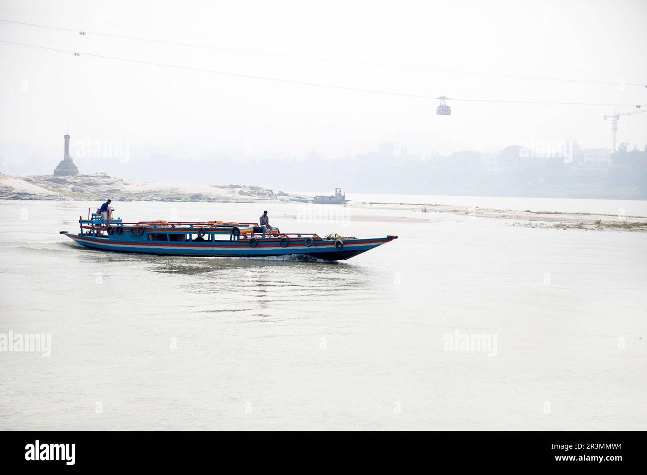 Bateau à passagers traditionnel en bois sur la rivière Brahmapoutre près de Guwahati avec un téléphérique au-dessus, reliant Guwahati à l'autre rive du fleuve, Assam, Inde Banque D'Images