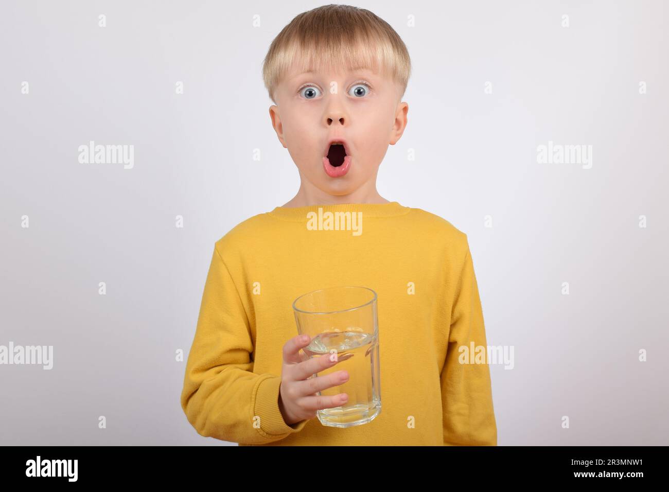 Un jeune garçon boit de l'eau claire provenant du verre Banque D'Images