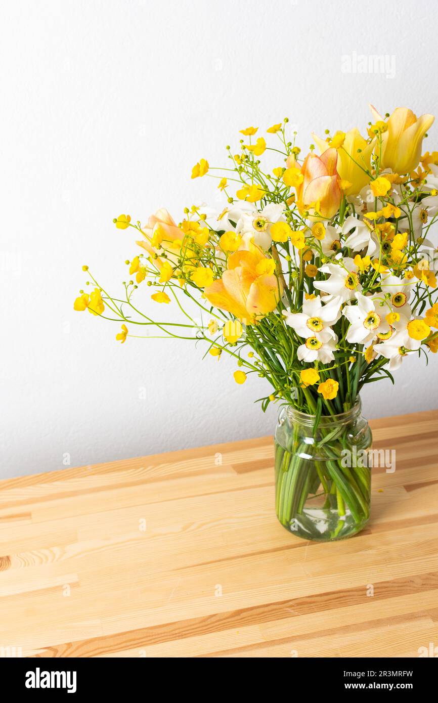 Bouquet printanier de buttertasses jaunes, jonquilles et tulipes blanches, bouquet de fleurs sur la table près du mur, décoration d'intérieur avec fleurs Banque D'Images