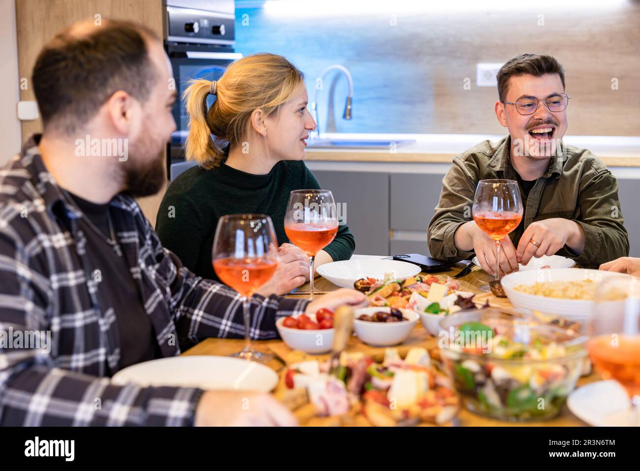Groupe d'amis dînant à la maison, en appréciant un bon rire dans un cadre confortable. Banque D'Images
