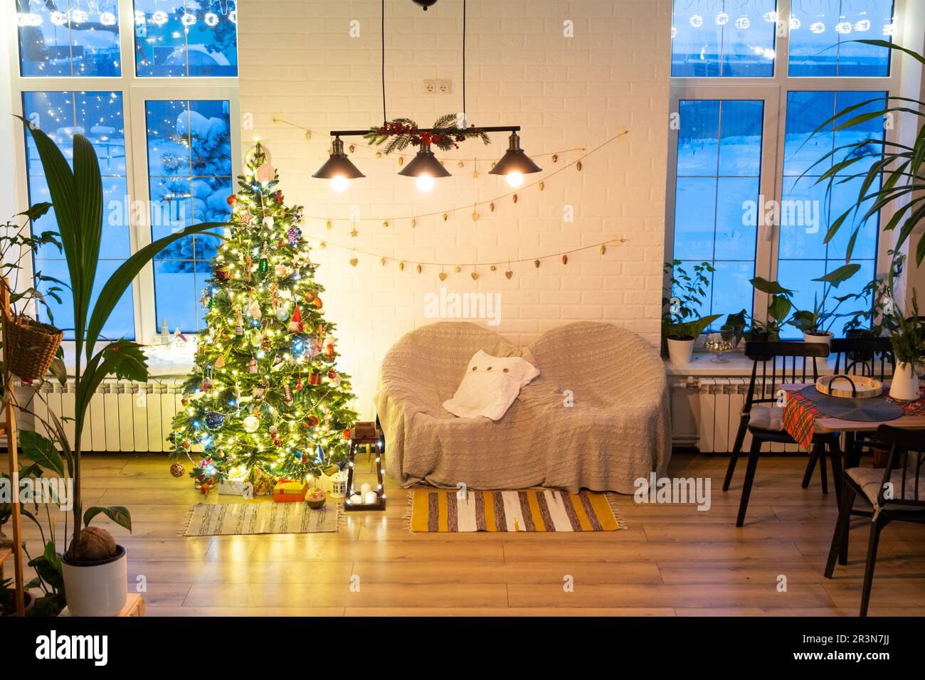 Arbre de Noël dans l'intérieur blanc d'une maison avec des murs de briques de style loft avec guirlande de jouets en verre sur une corde. Guirlande lumineuse de lumières de la décoration Banque D'Images